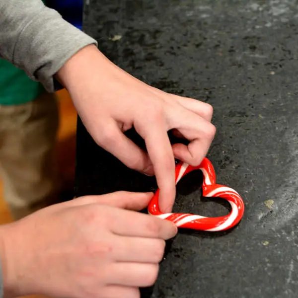 Hands shaping a warm candy cane into a heart